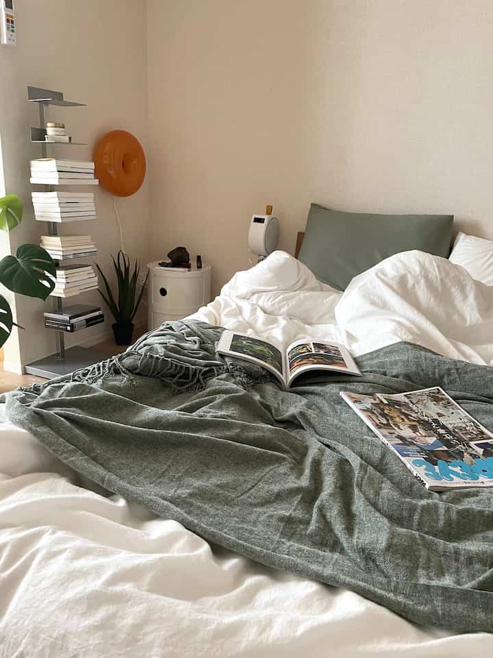 ベージュの壁と白い寝具、緑のブランケットと枕が配置されたナチュラルトーンの寝室のインテリア