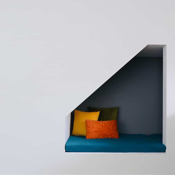 白い壁と青いクッションのヌック空間、黄色とオレンジのクッションがポイントのモダンな雰囲気のインテリア