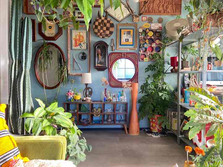 青い壁に多彩なヴィンテージウォールアートと観葉植物が配置されたナチュラルトーンのリビング