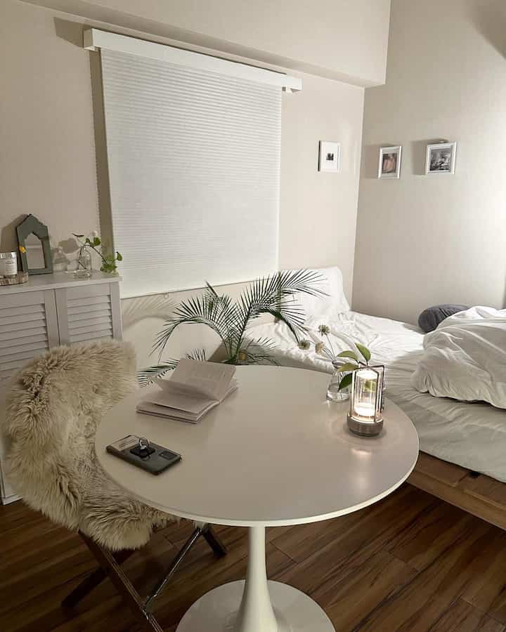 Bright white and wood-tone small cozy bedroom featuring a round table and plush chair with minimal decor