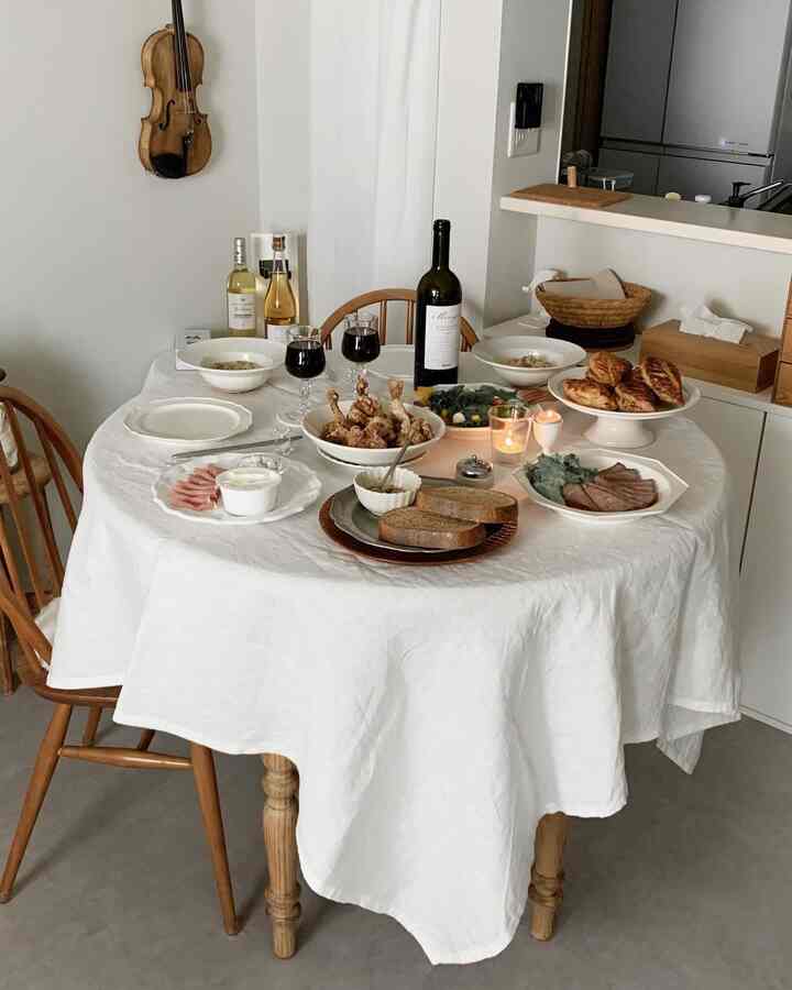 白のリネンテーブルクロスとナチュラルウッドの椅子が置かれたリビングの、クリスマスディナーがセッティングされた雰囲気のあるインテリア