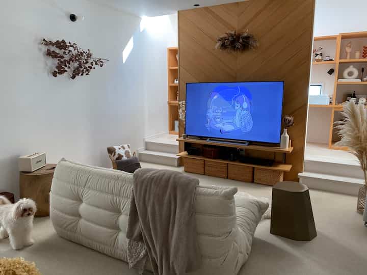 白と木目調が調和したリビング、ソファとスツールが配置され、落ち着いたミニマルな空間