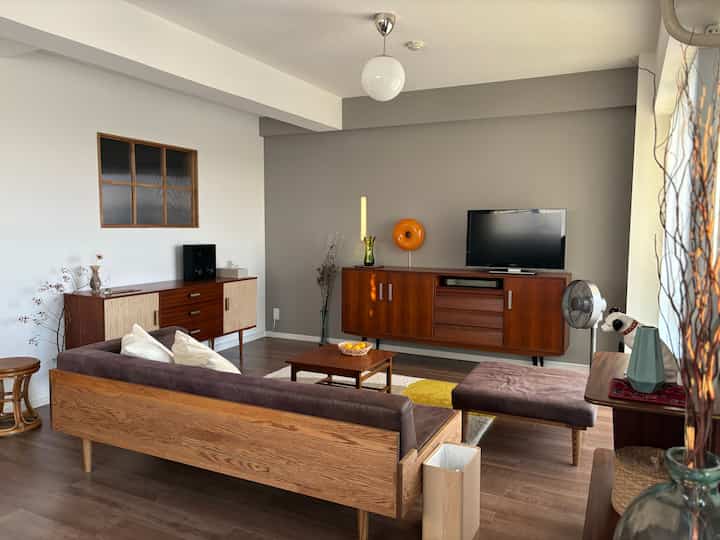 木目調とグレーの壁が調和したミッドセンチュリーモダンのリビング、ソファとテレビ台が配置された雰囲気のある空間