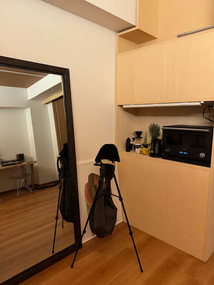 ナチュラルな木目調とブラックアクセントが調和する狭いワンルームのキッチンスペース、大きな鏡とコーヒー器具が配置された雰囲気のあるインテリア