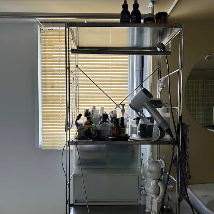 Bathroom with yellow blinds features stainless steel storage shelves and Dyson hair dryer beside the vanity in a natural setting