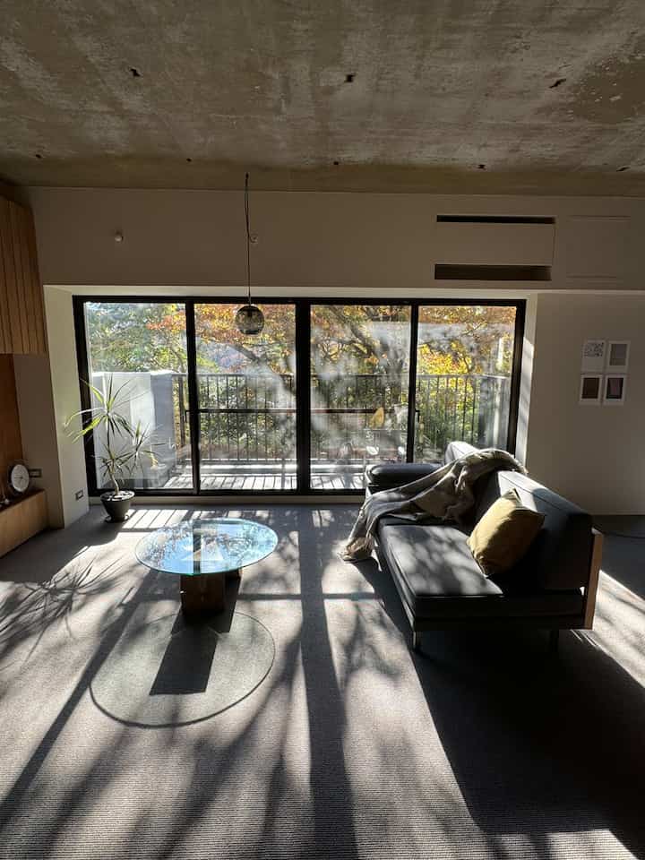 グレーと木目調のワンルームリビング、大きな窓から自然光が差し込み、温かみのある自然な雰囲気の空間