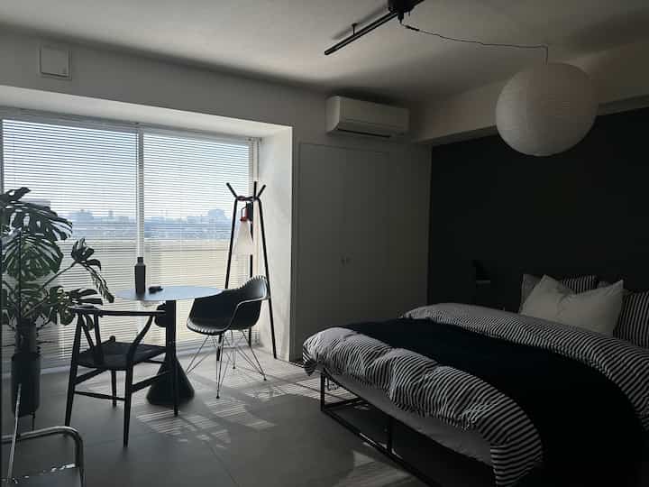 Modern black and white bedroom featuring large window-side dining table and armchair in a compact space