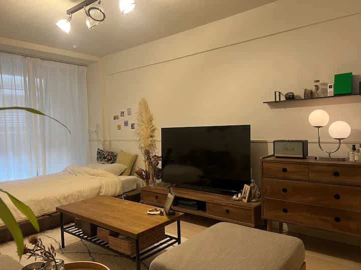 Beige-toned 1K studio apartment combining living and bedroom areas, featuring wood furniture and white bedding in a natural modern style