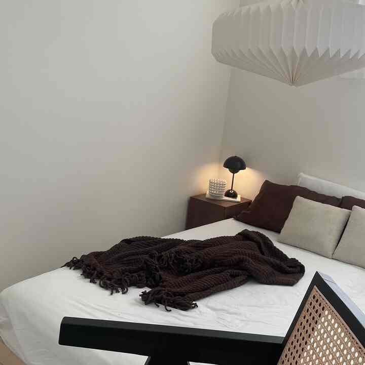 白と茶色が調和する寝室、シンプルなベッドとラタンチェアが自然で落ち着いた雰囲気を演出している