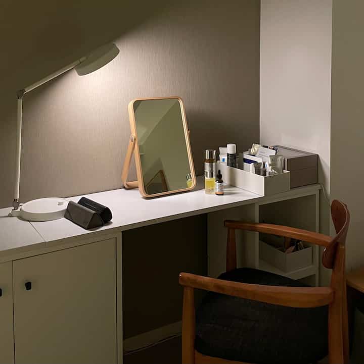 白と茶色のトーンのコンパクトなドレッサースペース、鏡と照明が配置されたDIYデスクとナチュラルな木製チェアのある落ち着いたインテリア