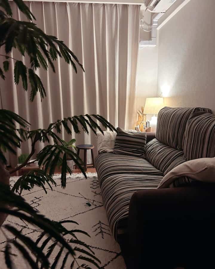 Cozy living room with beige curtains and brown sofa, warm lighting and plants creating a relaxing atmosphere