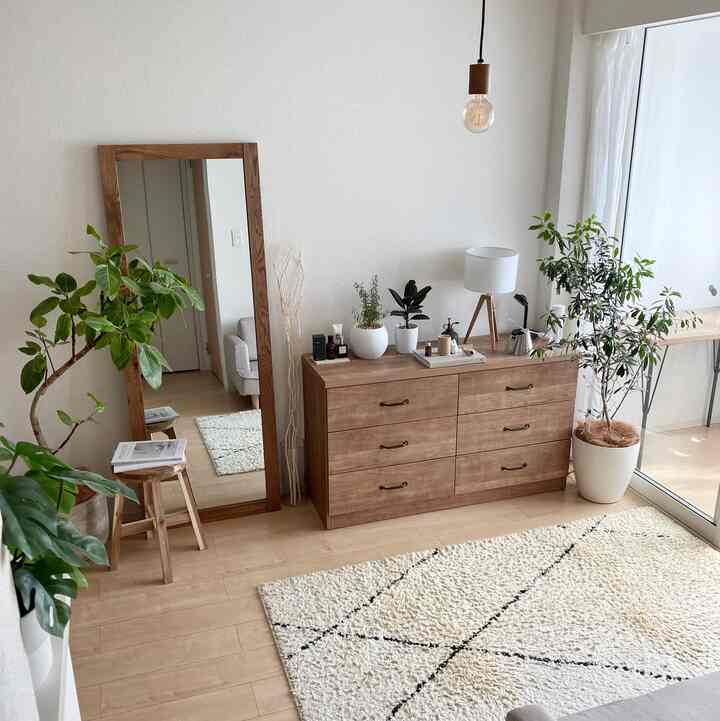 ナチュラルな木目調と白い壁が調和するリビング、木製の大きな鏡やチェスト、観葉植物が配置された落ち着きのあるインテリア