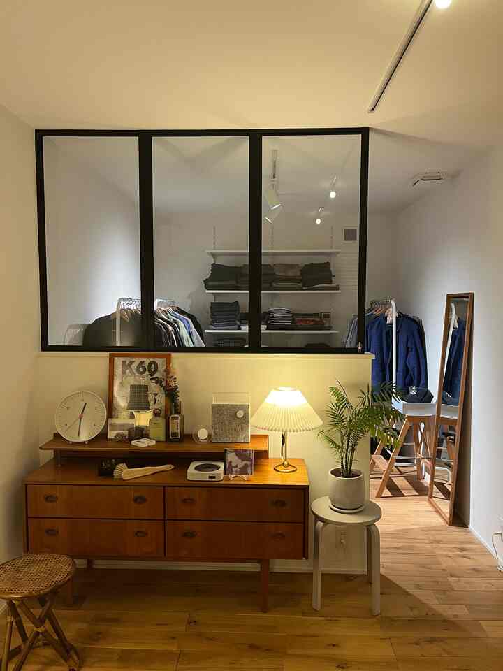 Natural tone living room featuring white walls, wooden sideboard, and a walk-in closet with clothes racks behind glass partition