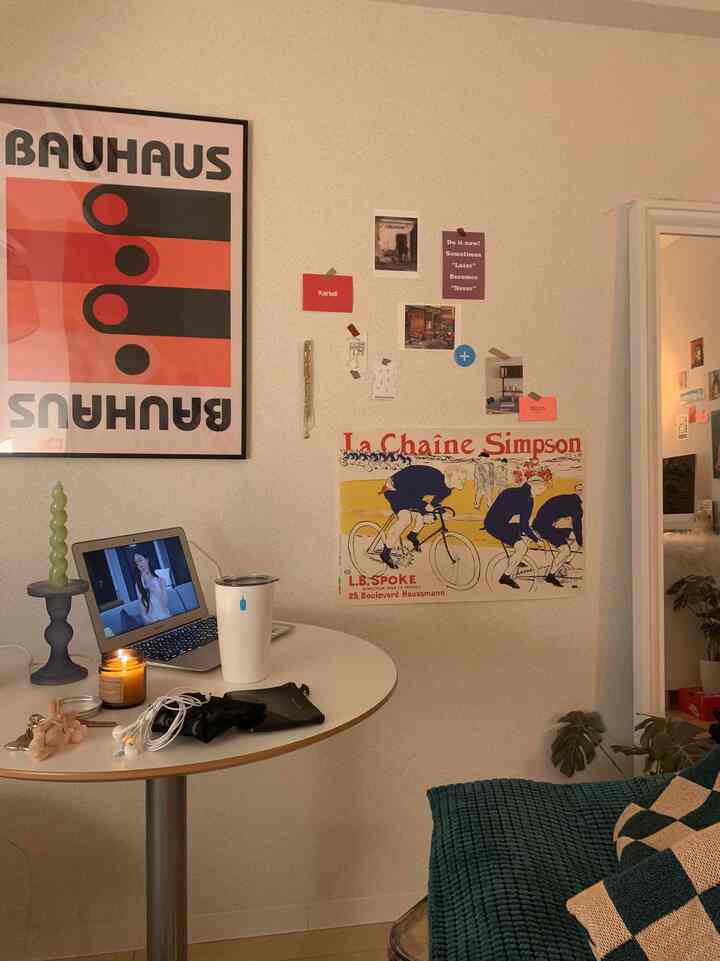 暖かい色調の壁、丸テーブルとターコイズのソファ、アートポスターが配置された一人暮らし向けのコンパクトな部屋