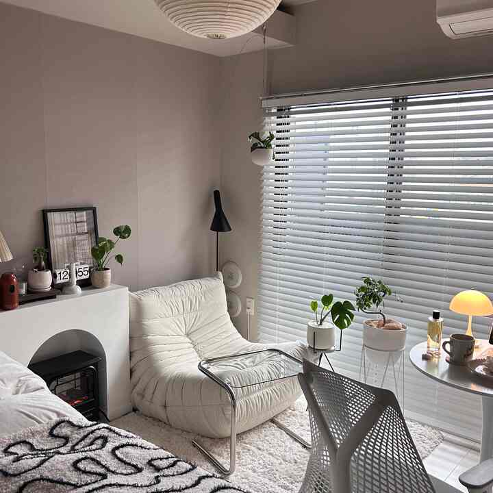 ナチュラルな色調のリビング、クリーム色のアームチェアとソファベッド、植物と白いブラインドが配置された雰囲気のある空間