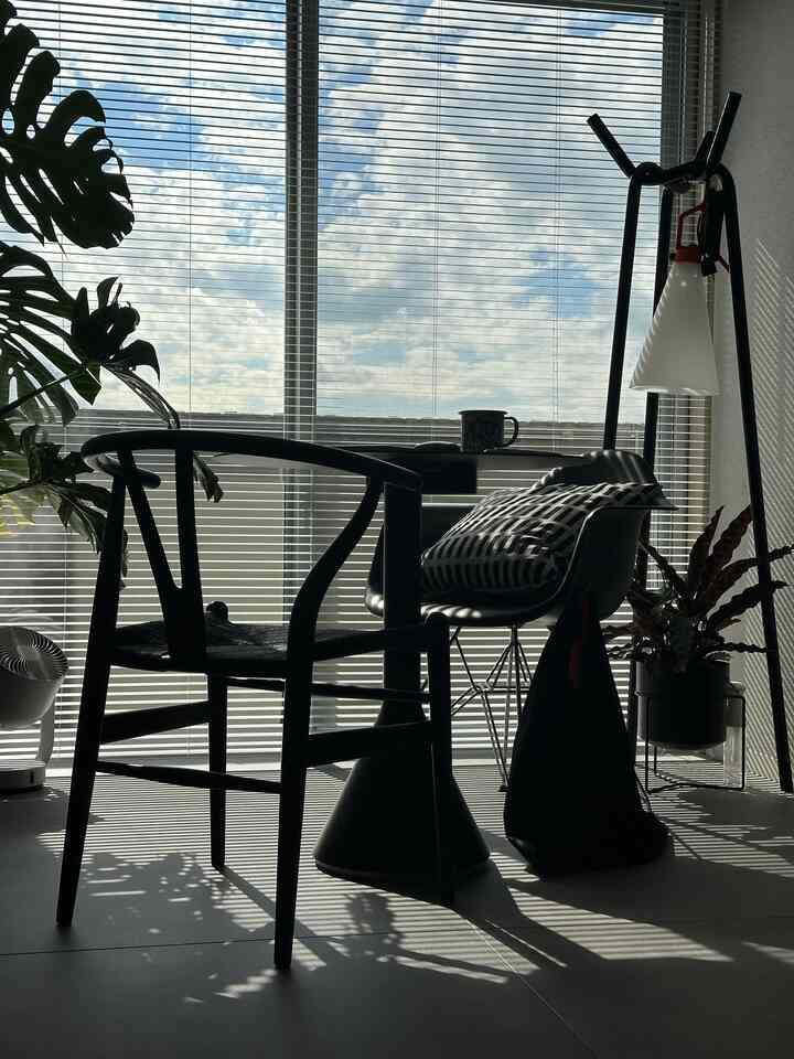 黒と白のトーンのバルコニー隣接の小さなダイニングスペース、アームチェアとダイニングテーブル、ブラインドが配置された落ち着いたモダンなインテリア