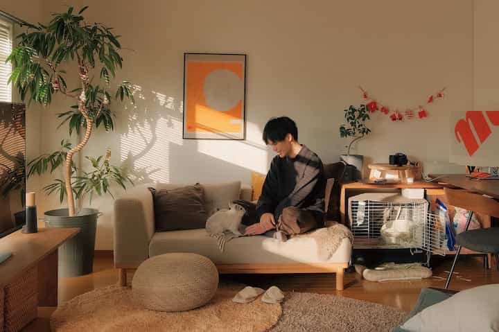 ベージュと木目調が調和した1LDKリビング、ソファに座る男性とうさぎがいる自然な雰囲気の空間