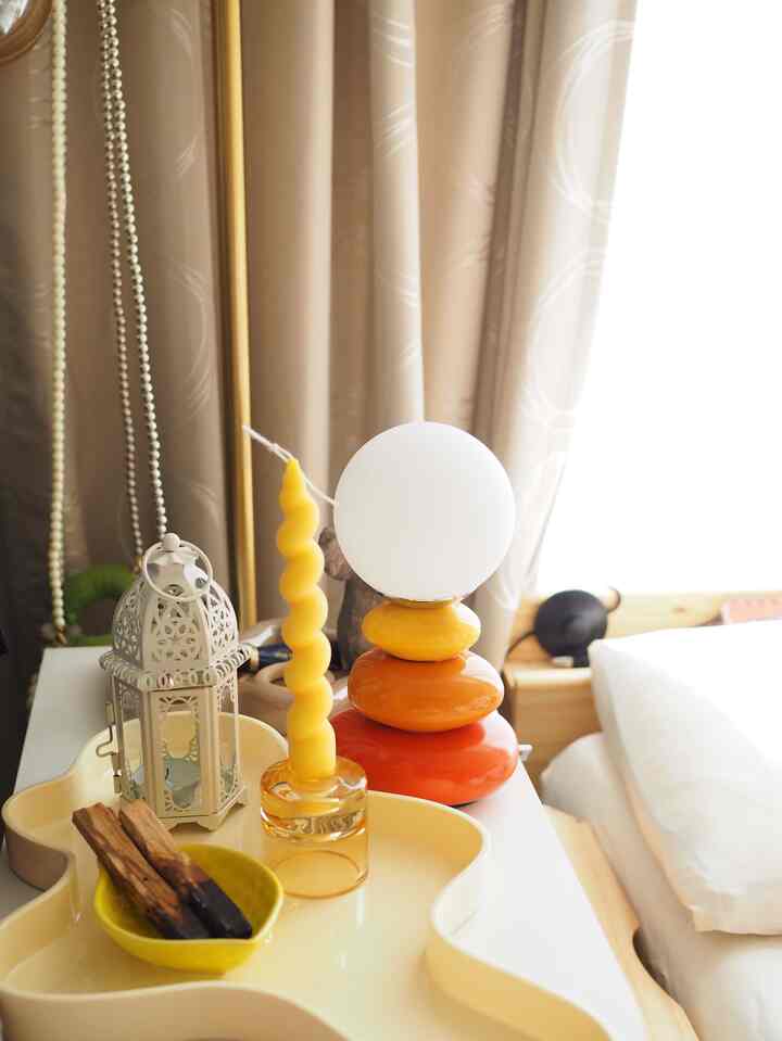 ベージュのカーテンと黄色いキャンドルがある寝室のテーブルランプとトレイが配置された自然な色調の空間