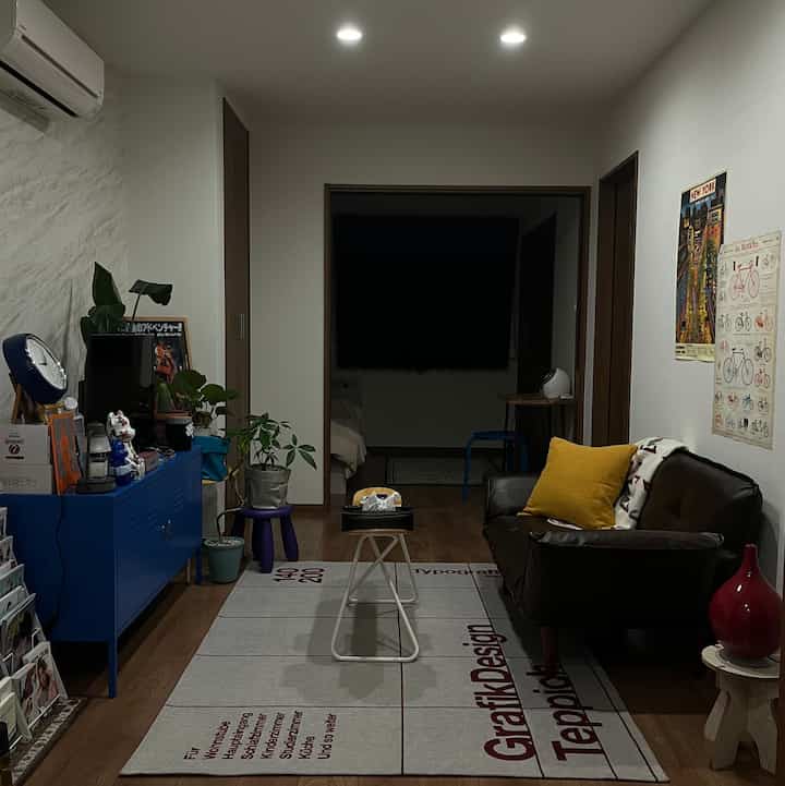 落ち着いたダークブラウンの革製ソファと鮮やかなブルーのスチールキャビネットが配置された、コンパクトな1LDKのリビングルーム。温かみのある印象的な空間