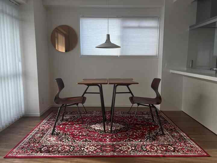 白を基調とした壁とブラウンの家具が調和するミッドセンチュリー風ダイニング、鮮やかなペルシャ絨毯の上にテーブルと椅子が配置された印象的な空間