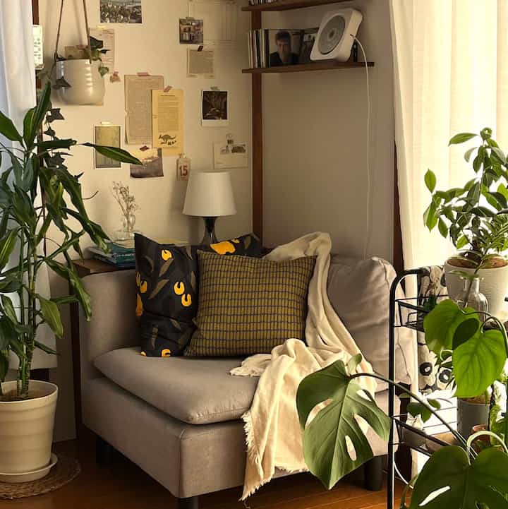 Natural-toned small living room featuring beige sofa with yellow patterned cushions and abundant green plants, creating a cozy atmosphere