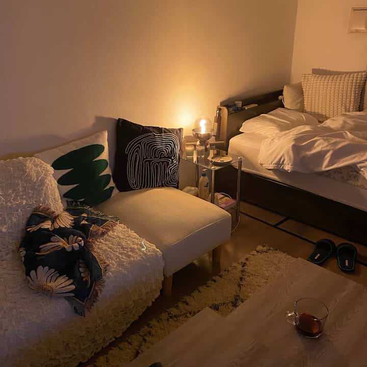 Cozy studio living and bedroom space with beige sofa and bed under warm lighting