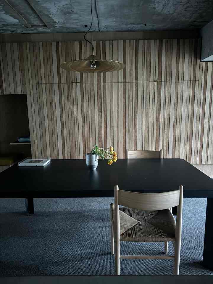 Modern natural dining room with wood tone wall, black dining table, and pendant light