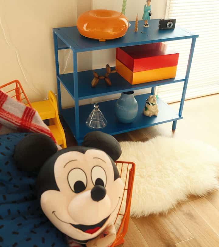 Cozy living room with warm natural light, blue shelving unit, and Mickey cushion in foreground