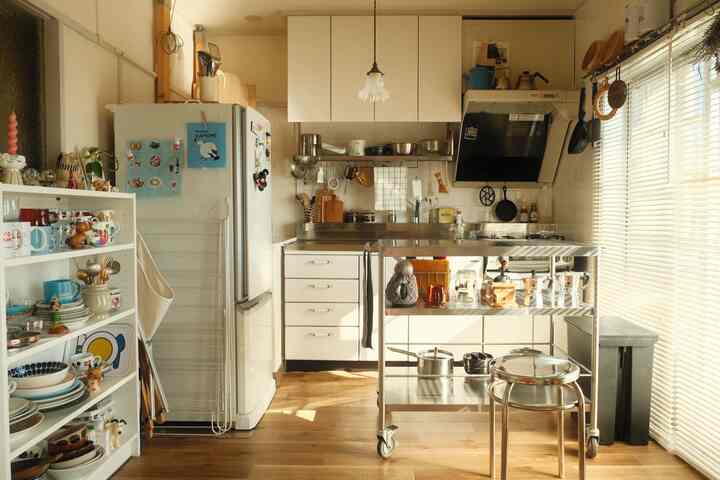 A compact kitchen in white and brown tones featuring stainless steel stool and kitchen cart with a natural warm atmosphere