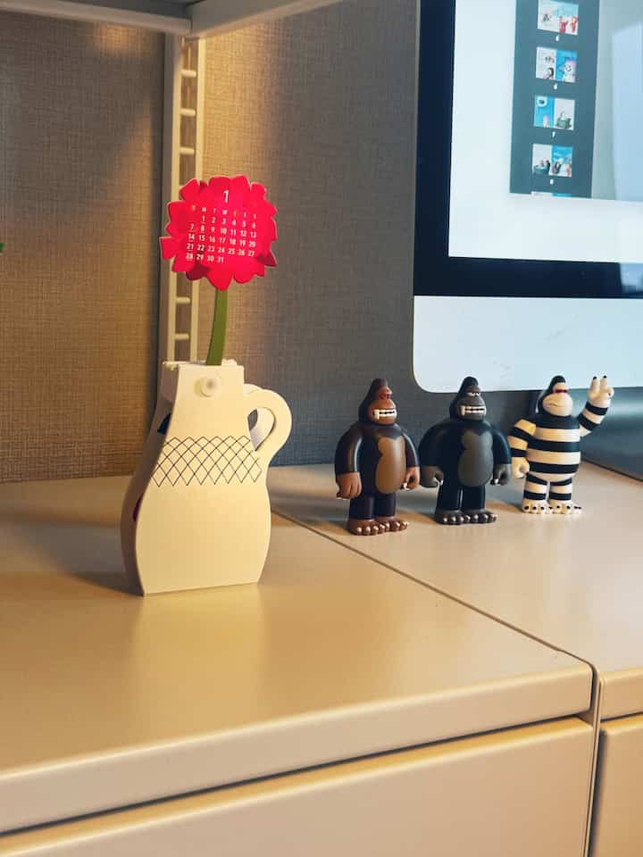 白いデスクの上に赤い花の形のカレンダーとゴリラのフィギュアが置かれたすっきりとしたホームオフィス空間