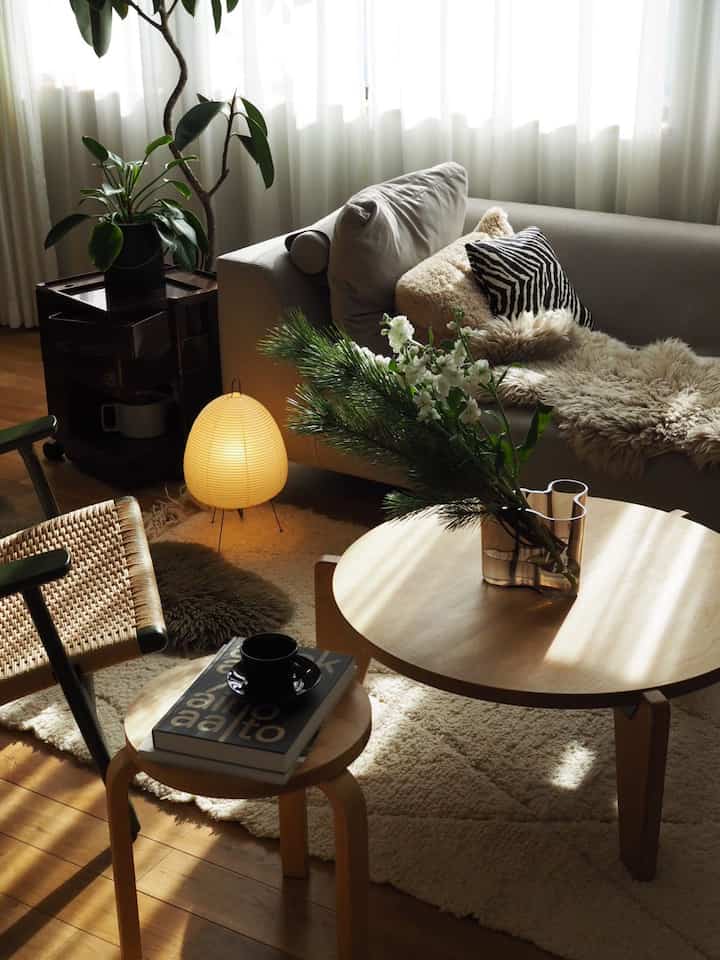 自然な木目調のリビング、グレーのソファと丸いコーヒーテーブル、植物が配置された雰囲気のある空間