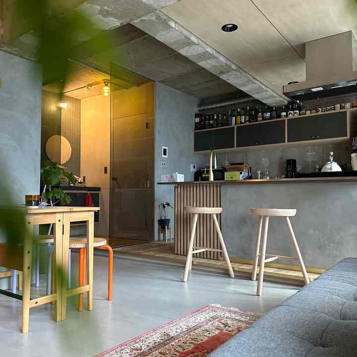 ナチュラルな色調のコンクリート壁と木製スツールが配置されたモダンなリビングとキッチンの空間