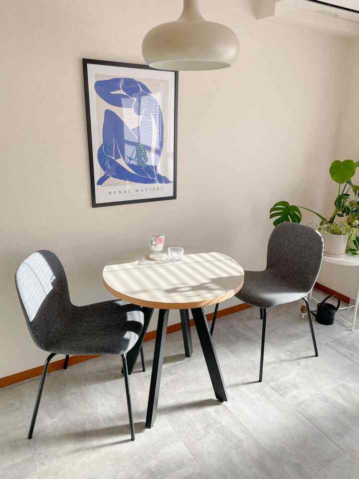 Bright white-toned dining room featuring a round dining table with two gray chairs, arranged neatly in a clean space