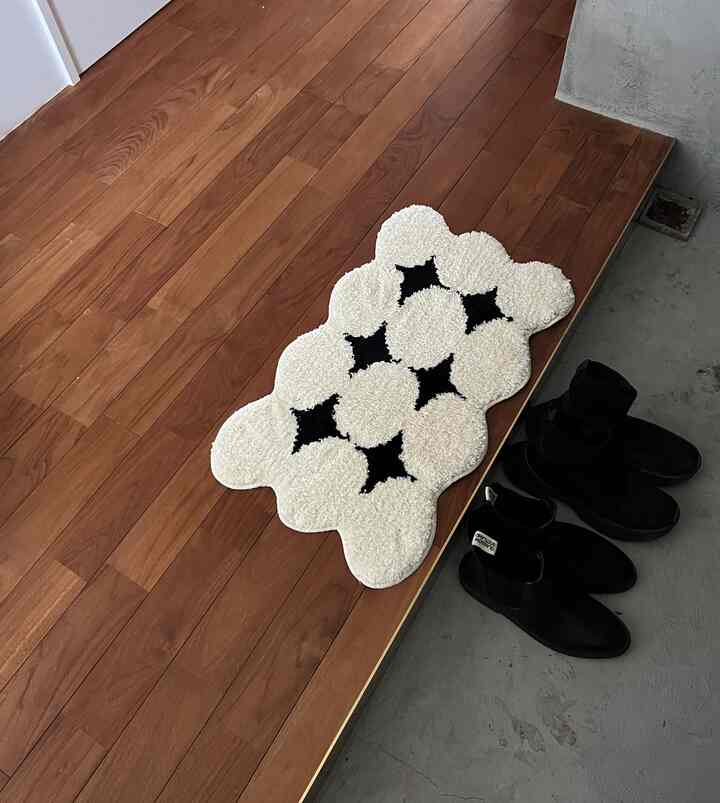 Modern balcony space featuring brown wooden flooring and a uniquely patterned black and white rug, with shoes placed alongside