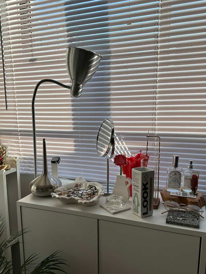 白い収納キャビネットの上にシルバーのディフューザーやメタルランプ、丸い鏡などが置かれたブラインド背景の整った空間