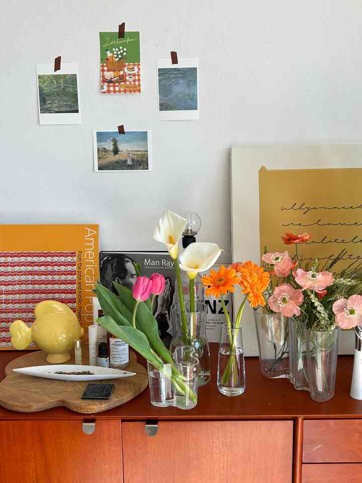 白い壁と暖かみのある木目調キャビネットの上に様々な花瓶と花が飾られたナチュラルで印象的なインテリア