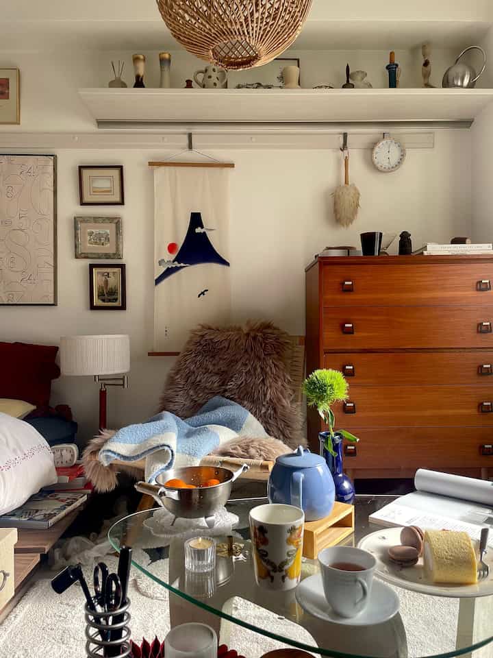 Natural tone living room featuring wooden dresser, table lamp, and cozy home cafe setup with tea set and blanket