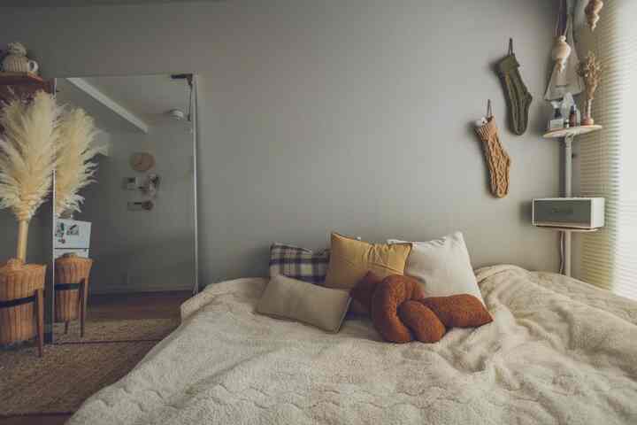 ベージュとナチュラルな色調の寝室、快適な寝具とクッション、壁の装飾とスピーカーが配置された雰囲気のあるインテリア