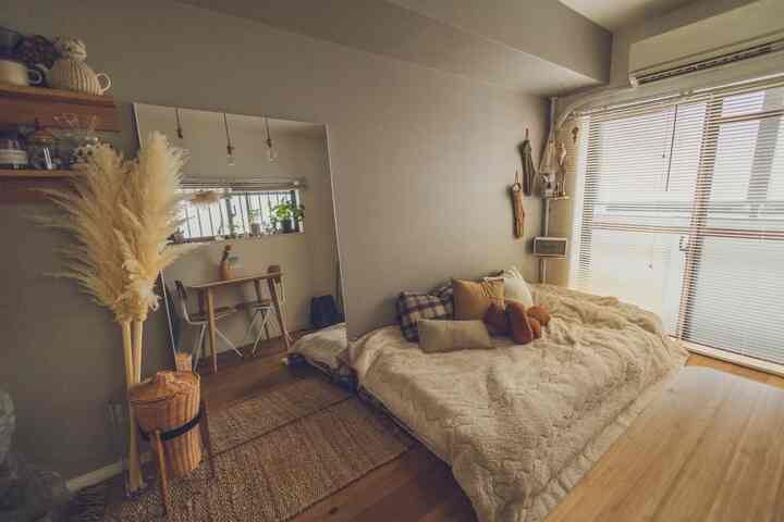 A cozy bedroom featuring beige tones and wood accents, with a plush bed, large floor mirror, and natural fiber rug