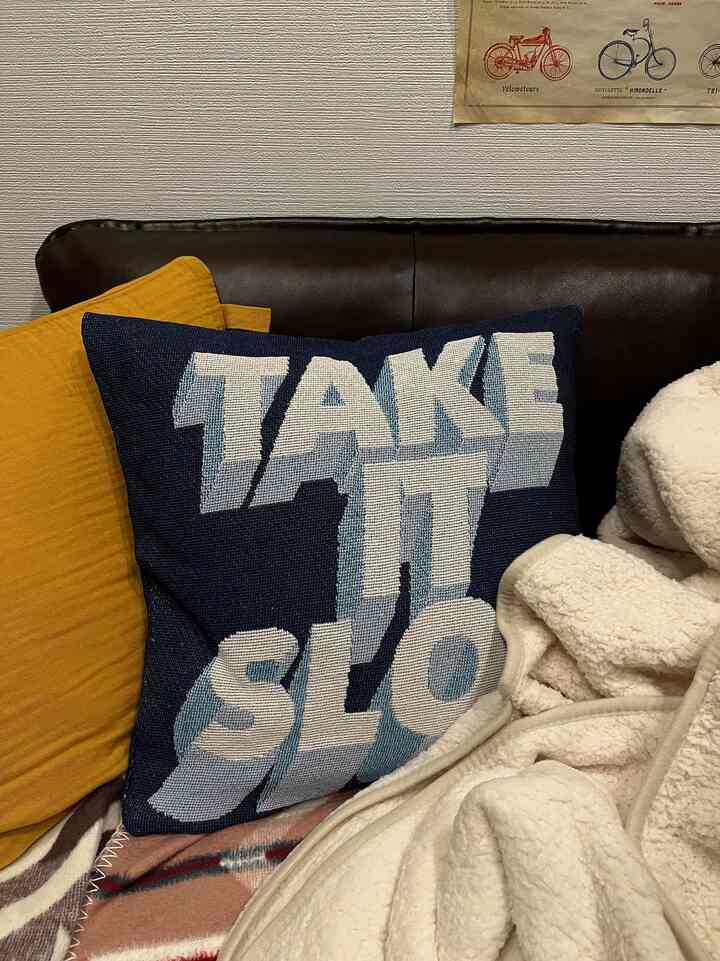 ネイビーとブラウンの色調のリビング、ネイビーの『TAKE IT SLOW』クッションとマスタードクッション、アイボリーのスローが配置された落ち着いた空間