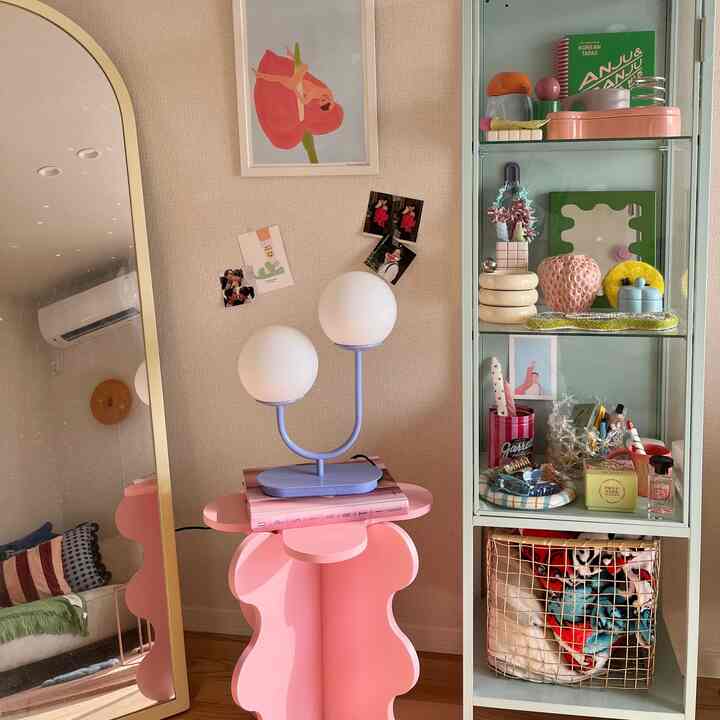 アイボリー色の壁にピンクの彫刻的サイドテーブルと青いテーブルランプが配置された雰囲気のある空間