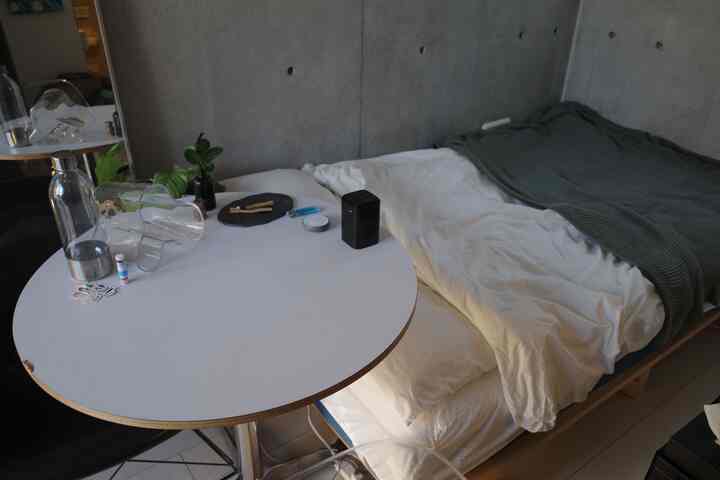 白とグレーのトーンのワンルーム寝室、丸テーブルとベッドが配置された落ち着いた空間