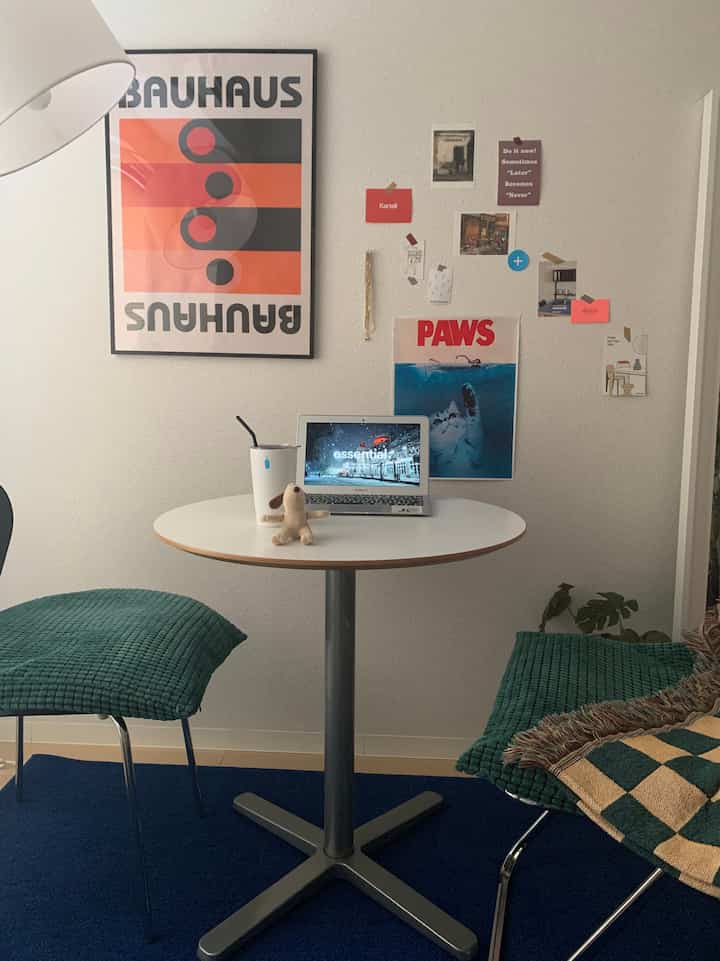 白と青の色調のリビングルーム、丸いテーブルと緑色のクッション椅子2脚が配置された落ち着いた空間