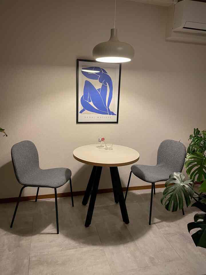 ベージュ色調の落ち着いたダイニングルーム、丸テーブルとグレーのチェア2脚、ペンダントライトが温かな雰囲気を作る空間