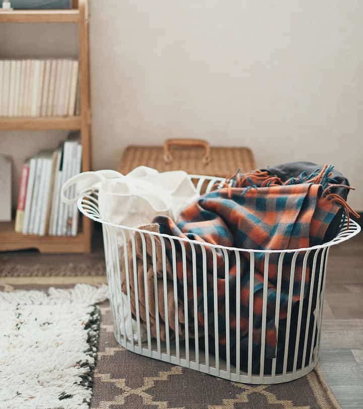 A cozy space featuring a white basket filled with blankets placed on the natural-toned living room floor