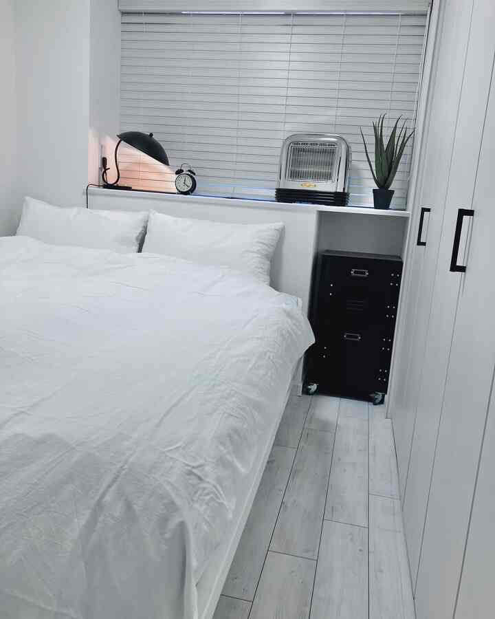 白と黒のモノトーン調インダストリアル寝室、白いベッドと黒いメタルチェスト、ブラインドのある窓が配置された清潔感のあるインテリア