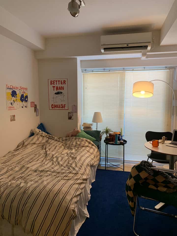 ブルーのトーンのワンルーム寝室、ストライプの寝具と丸いテーブルが配置された温かみのある空間