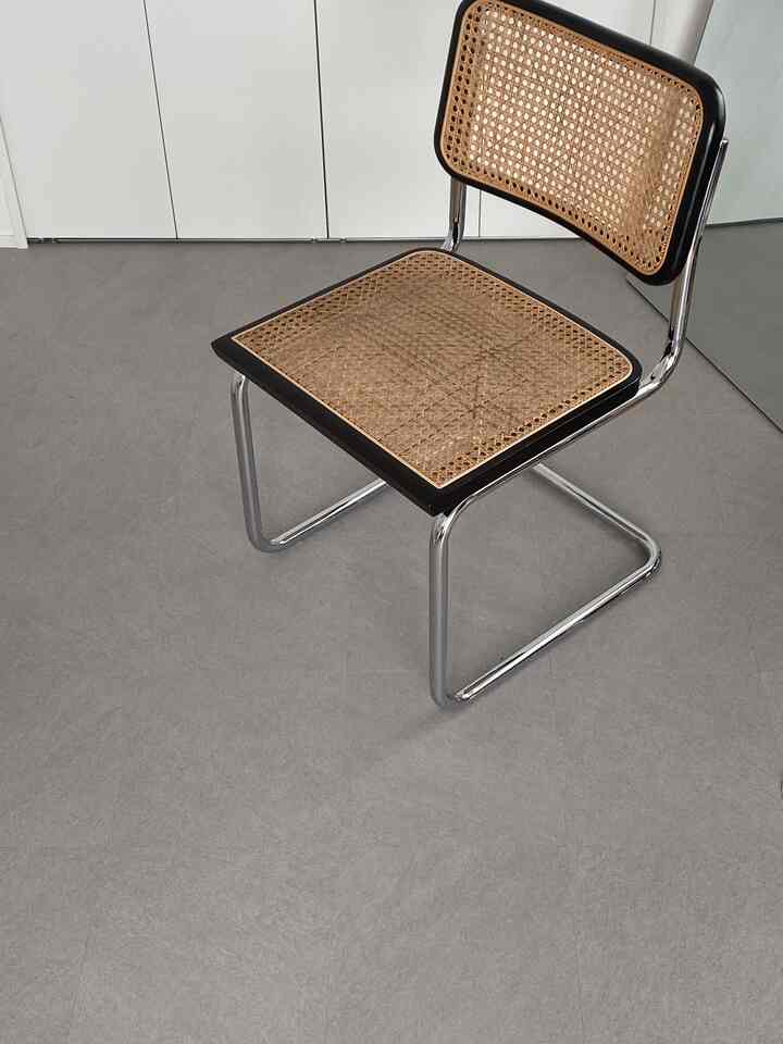 ナチュラルなグレー色調のウォークインクローゼット、クロームフレームと籐の座面が特徴のモダンな椅子が配置された空間