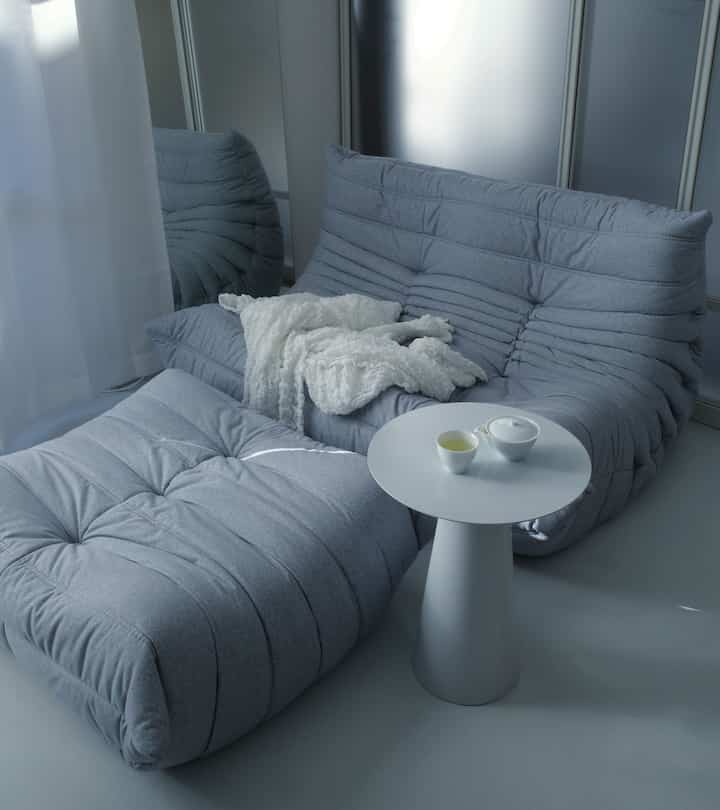 ブルーとグレーの落ち着いたトーンのコンパクトなリビング、ふかふかのソファとサイドテーブルにお茶セットが置かれた雰囲気のある空間