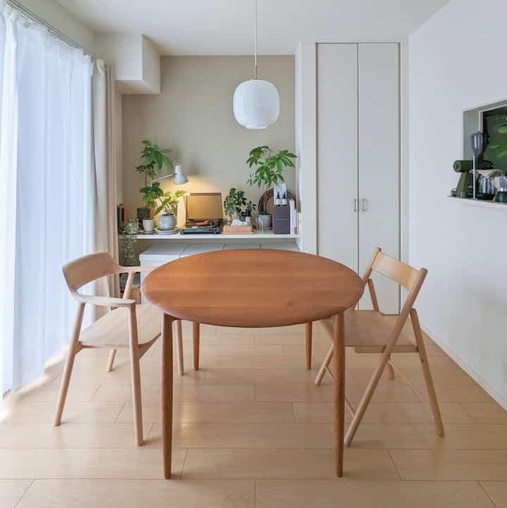 Natural and white toned dining room featuring a round wooden dining table, armchair, and pendant light in a simple setting